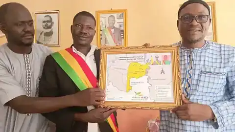 Remise d'un tableau encadré de la carte de la commune de Tiongui à une autorité, entre deux responsables